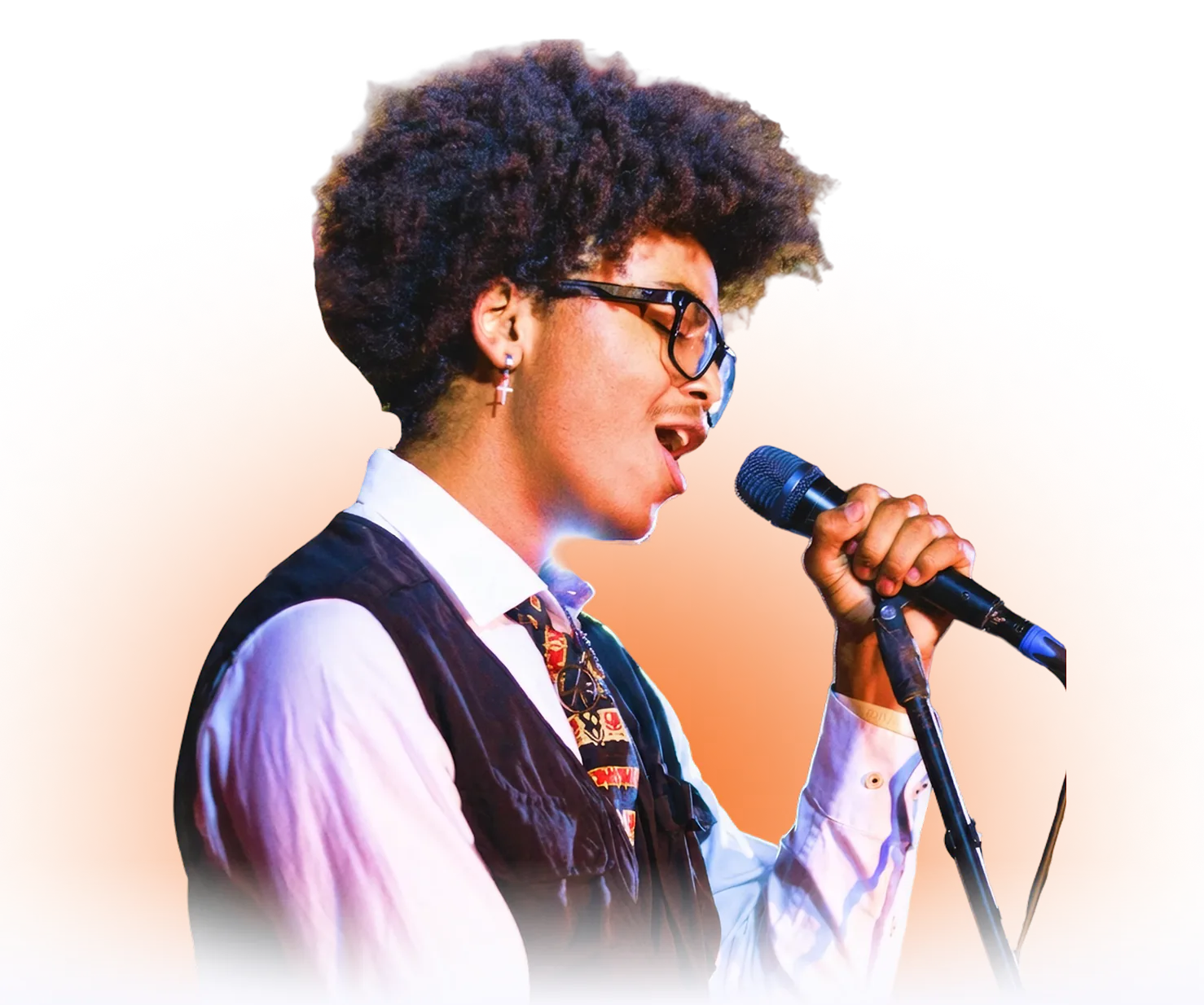 Young musician with curly hair and glasses singing into a microphone while wearing a white shirt, tie, and dark vest.